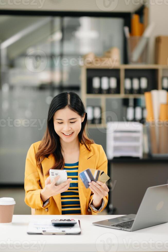 Asian Woman using smart phone for mobile payments online shopping, omni channel, sitting on table, virtual icons graphics interface screen photo