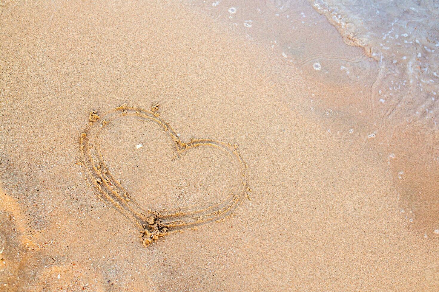 Finger drawing on the sand. The heart is painted on the beach near the oeyan. Happy holiday by the sea. photo