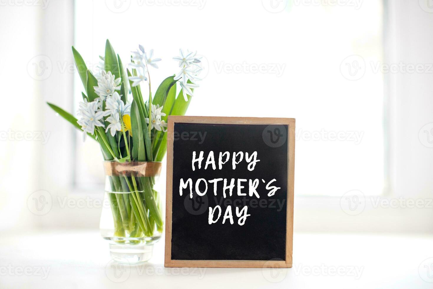 Fresh blue spring flowers Scilla siberica and wooden blackboard with sample text Happy Mothers Day near the window photo