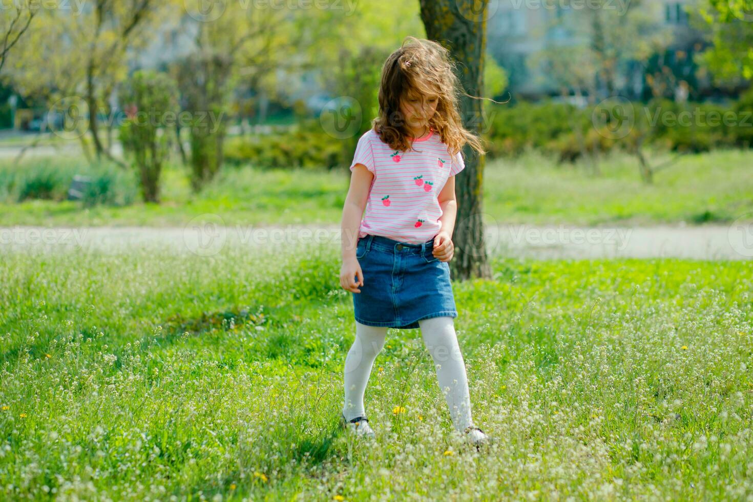 beautiful little girl with developing hair walks in street violating quarantine of coronavirus. girl in pink T-shirt runs across green field. girl plays active games in nature in summer or spring. photo