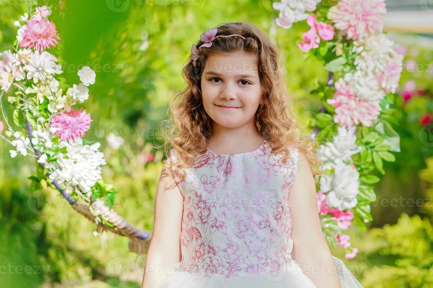 a little girl in a pink dress standing in front of a floral wreath photo