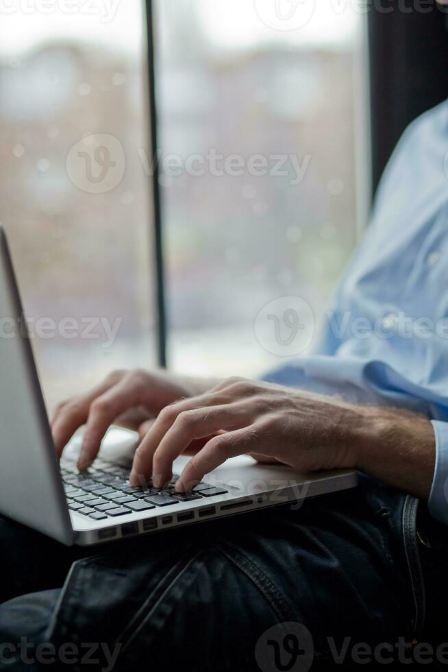 A man sits on a windowsill and works on a laptop. Beautiful man's wrist. Long fingers of a young man. photo