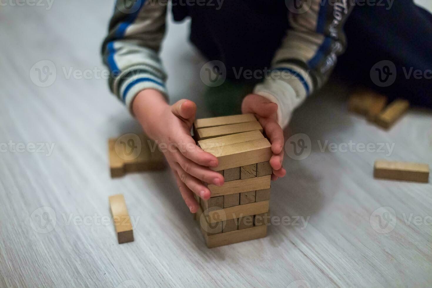 el niño construye un torre de de madera bloques torre juego con un de madera. madera bloquear apilado como paso movimiento.de.escalera borroso suave atención foto