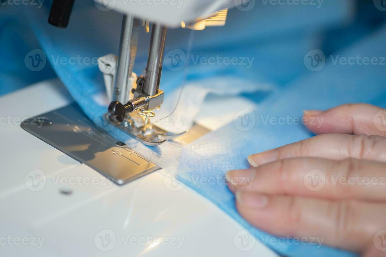 Sewing Homemade protective medical mask in process. woman holds a spunbond, sms, Meltblown mask at home. Detail White modern sewing machine and three-layer masks. photo