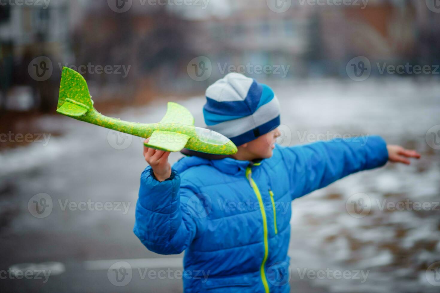 The boy launches a glider plane green in winter. Active games on the air. Airplane flights. Traveling in the winter. photo