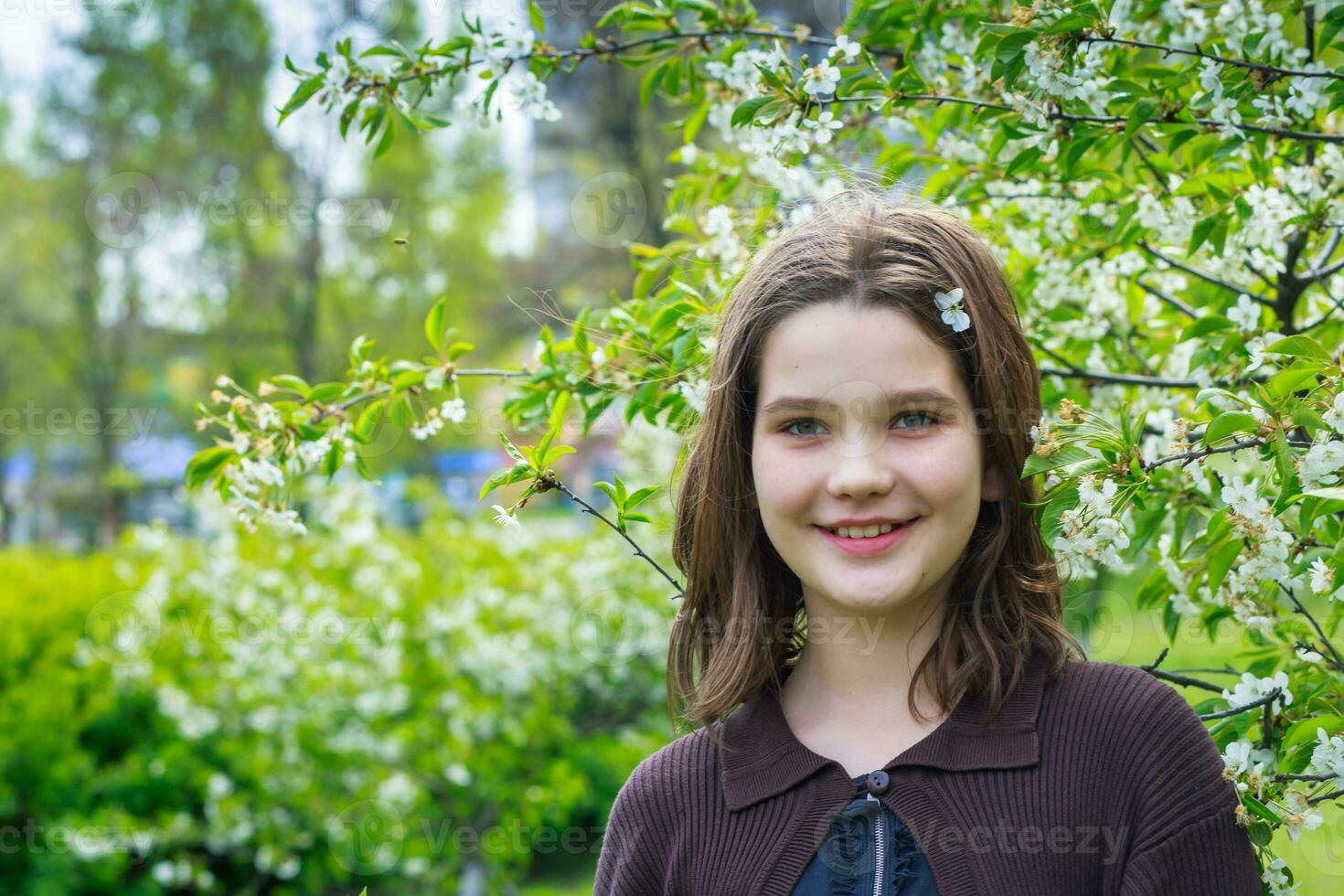 hermosa niña entre Cereza flores en primavera. retrato de un niña con marrón pelo y verde ojos. foto