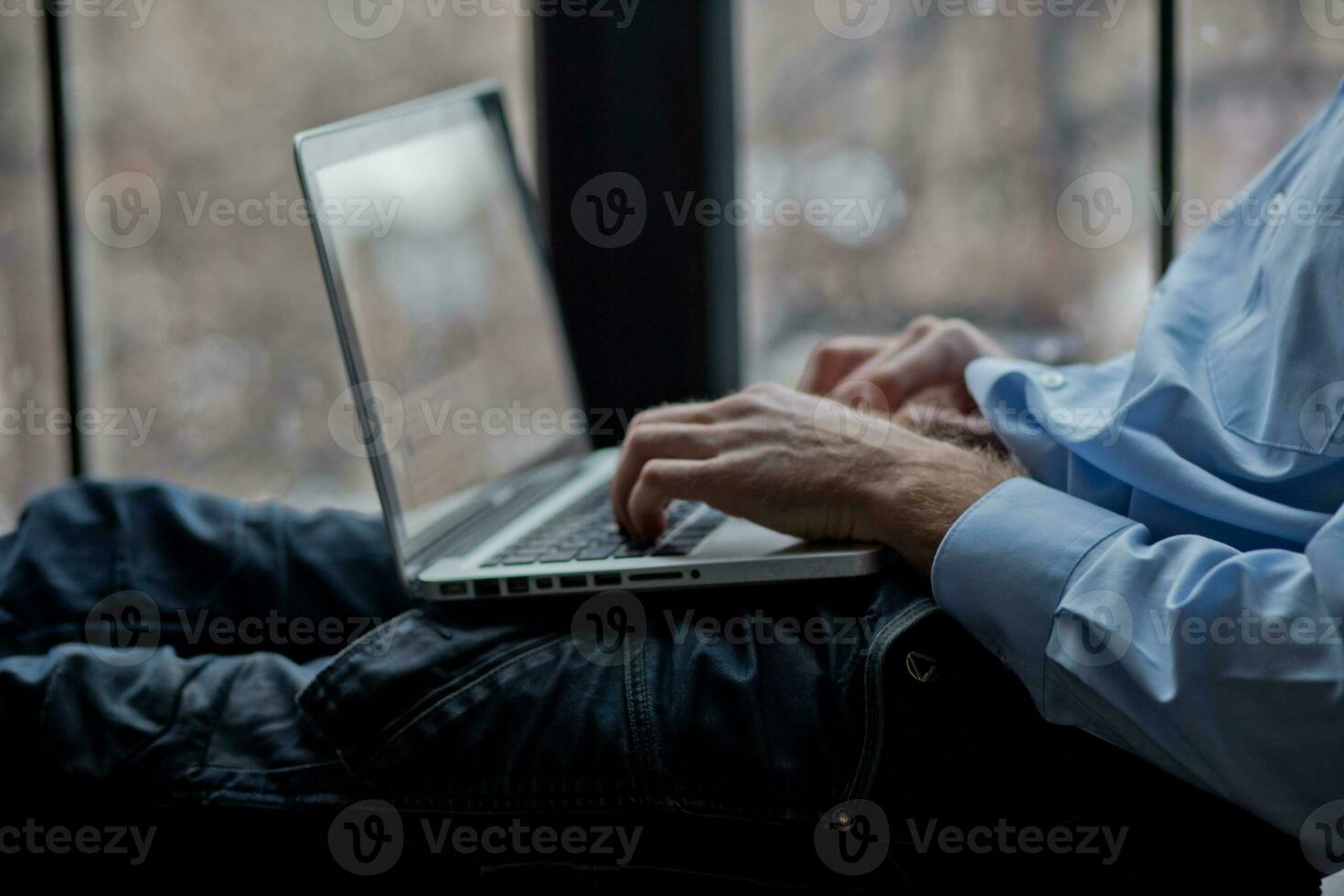 A man sits on a windowsill and works on a laptop. Beautiful man's wrist. Long fingers of a young man. photo