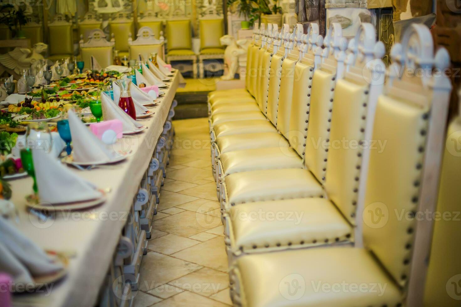 Beautifully served table for a banquet in a restaurant. White napkins and blue and green wine glasses on the table. A number of old chairs photo