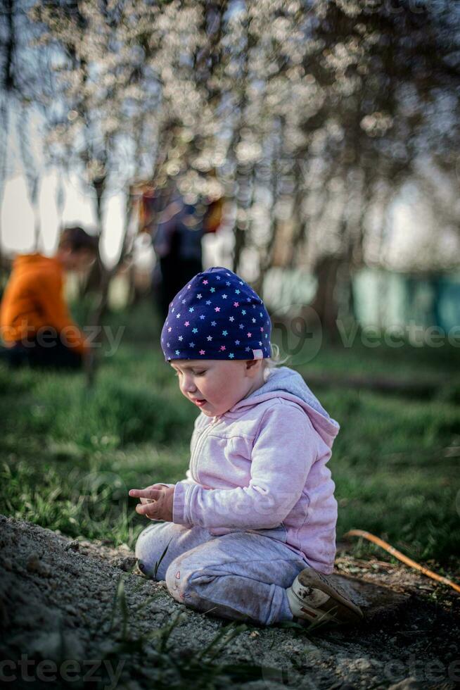 A little girl sits on a pile of soil in the village. A child plays in the backyard of a house. photo