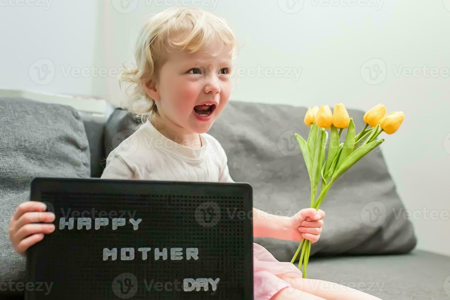 little girl holds a bouquet of yellow tulips and a sign that says Happy Mother's Day. child gives flowers to mother for holiday. photo