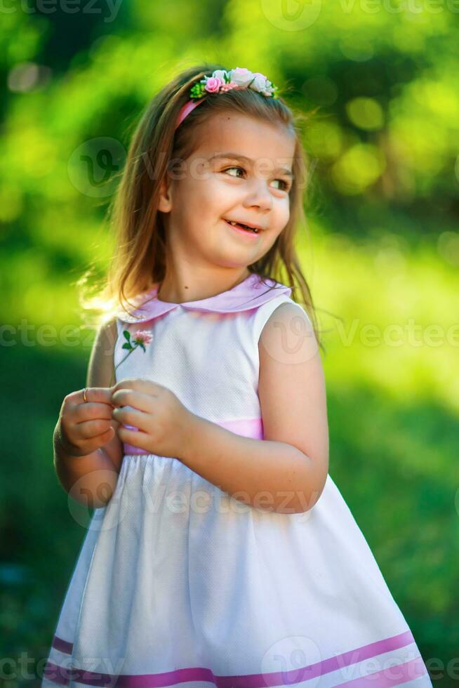Beautiful girl smiling and holding a flower clover. A small child on a background of green bushes. photo