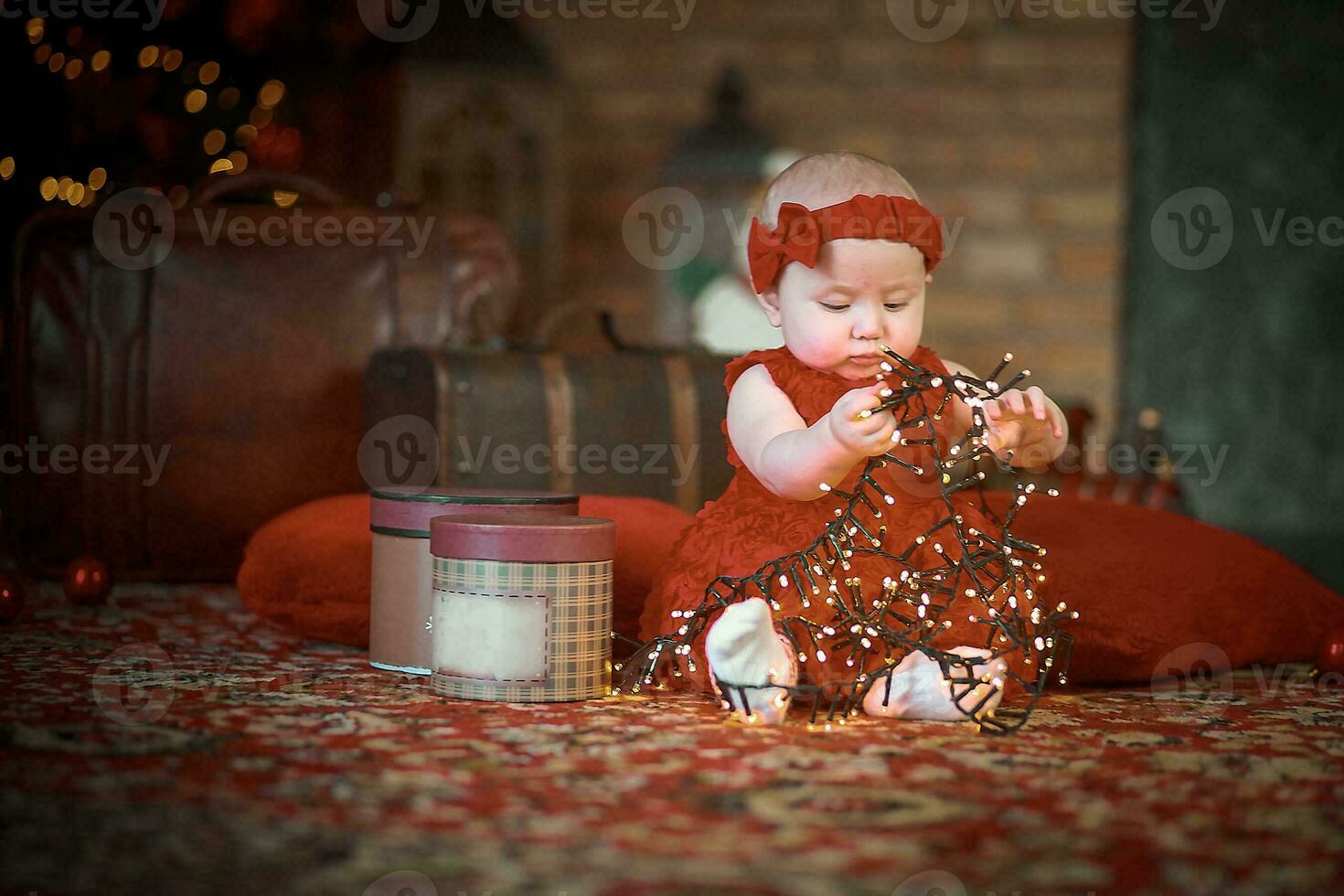 little girl in red dress against background of Christmas tree holds Christmas garland in her hands. baby 6 month old celebrates Christmas. photo