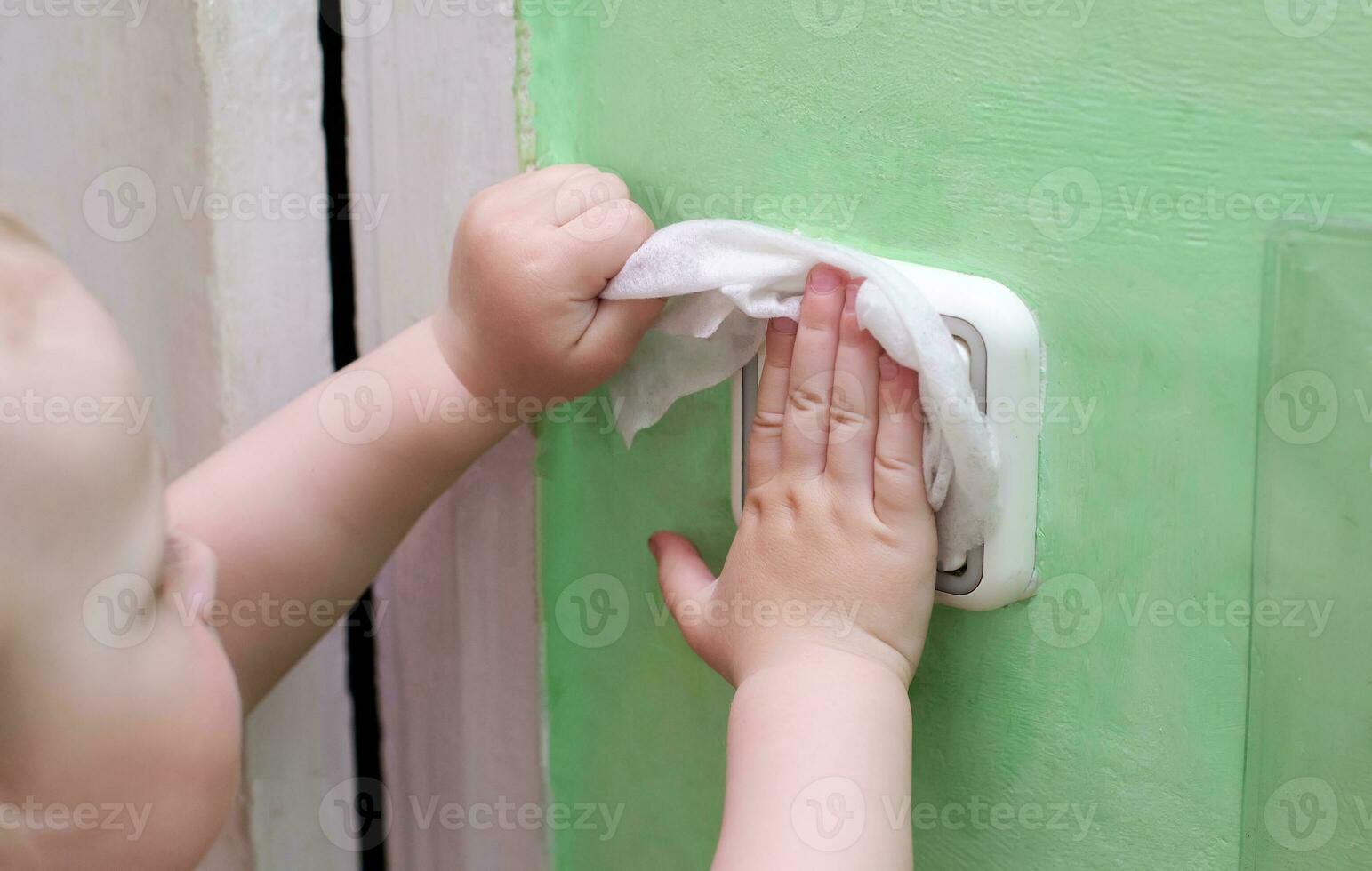 little girl wipes light switch on wall with wet cloth. Protection from coronavirus. Sterile conditions at home. Cleaning house, cleaning up viruses. Early spring cleaning or regular clean up photo