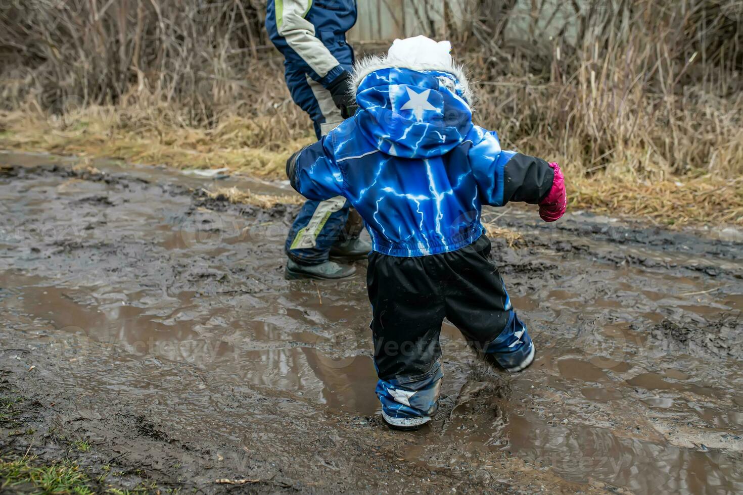 The child is trying to cross the road with mud and puddles on a country road. PRogulianka after a thaw in the spring on the way with dirt photo