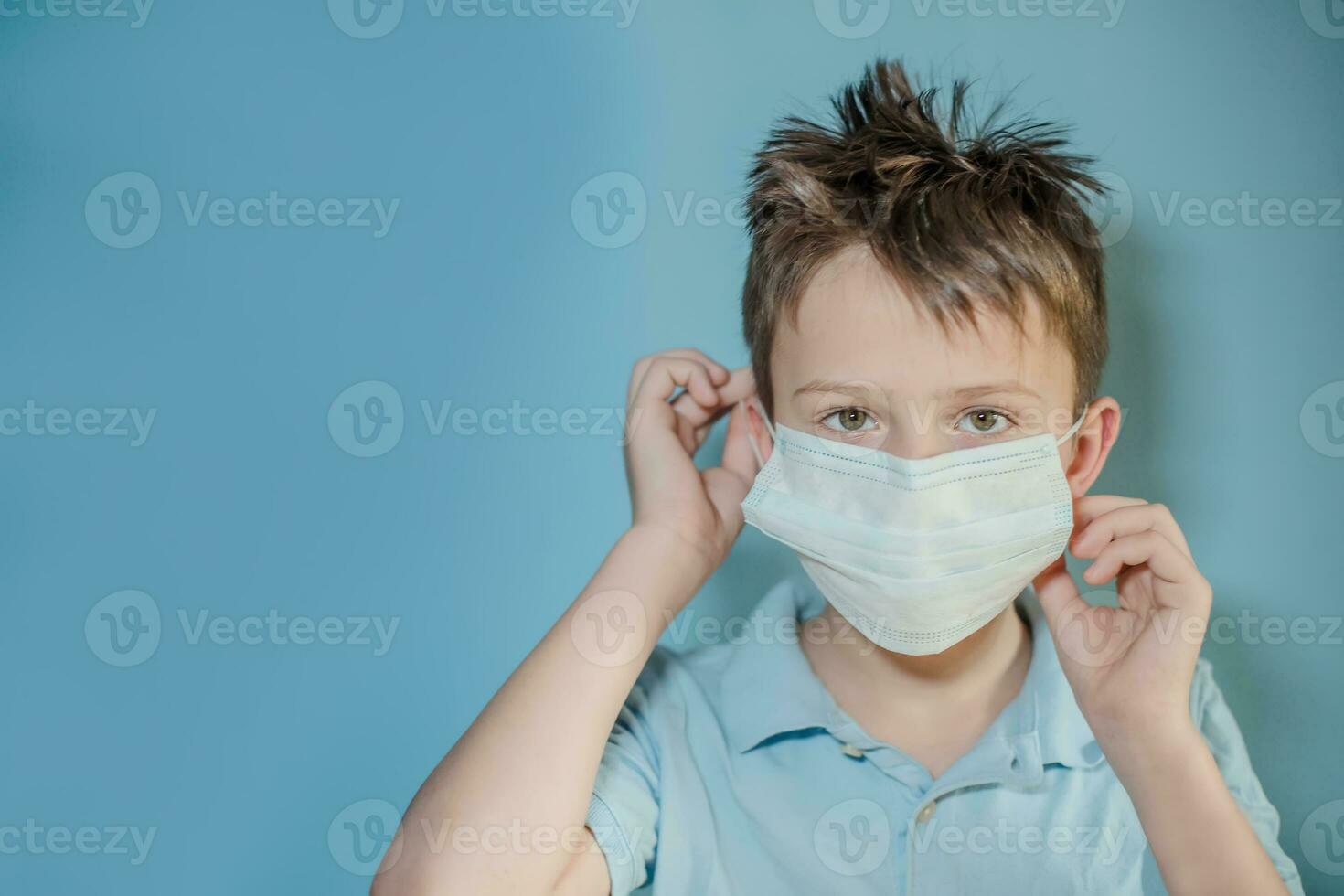 boy removes protective medical mask from face on blue background. child with flu, hantavirus or cold protected from viruses, pollution in bad epidemic situation, among patients with coronavirus photo