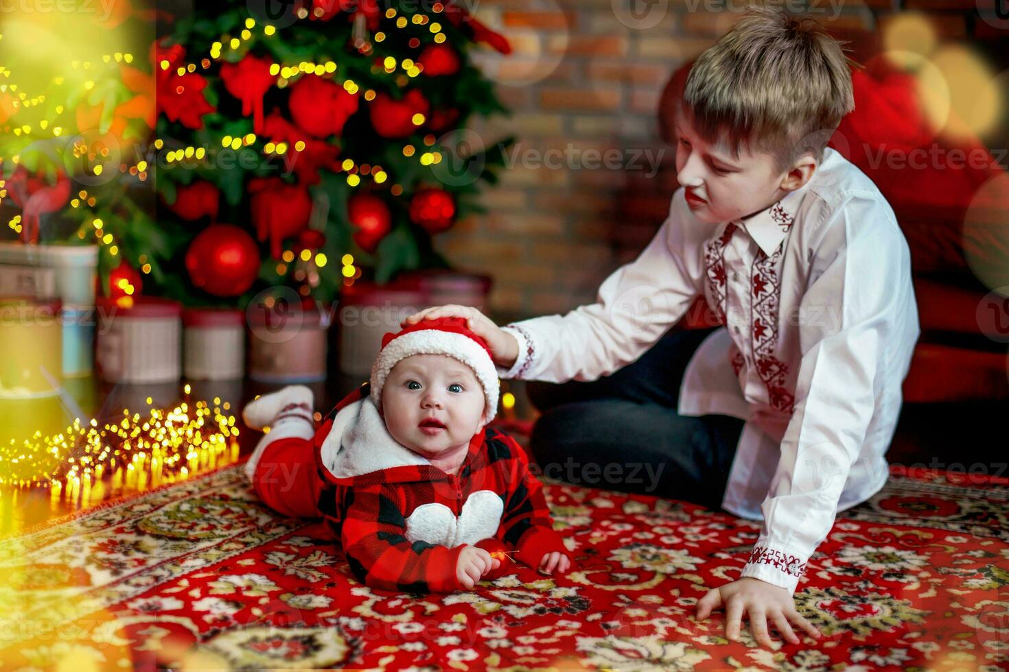 hermano con pequeño hermana a el nuevo año árbol. familia celebra Navidad. 6 6 meses antiguo pequeño chico aprende a gatear foto