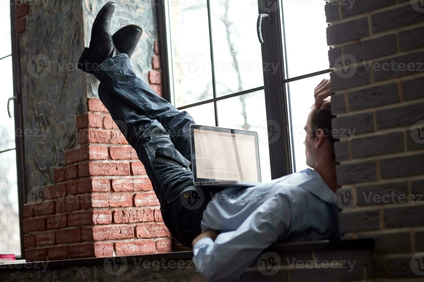 A man sits on a windowsill and works on a laptop. Beautiful man's wrist. Long fingers of a young man. photo
