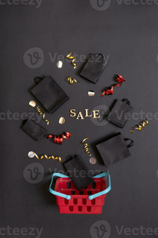 Sale text and shopping bags and shopping cart with festive decorations on black background flat lay, top view. Black friday sale concept. photo