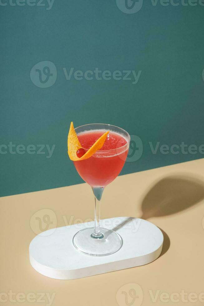 Pink alcoholic cocktail in steamed glasse on white podium or pedestal on colored background photo