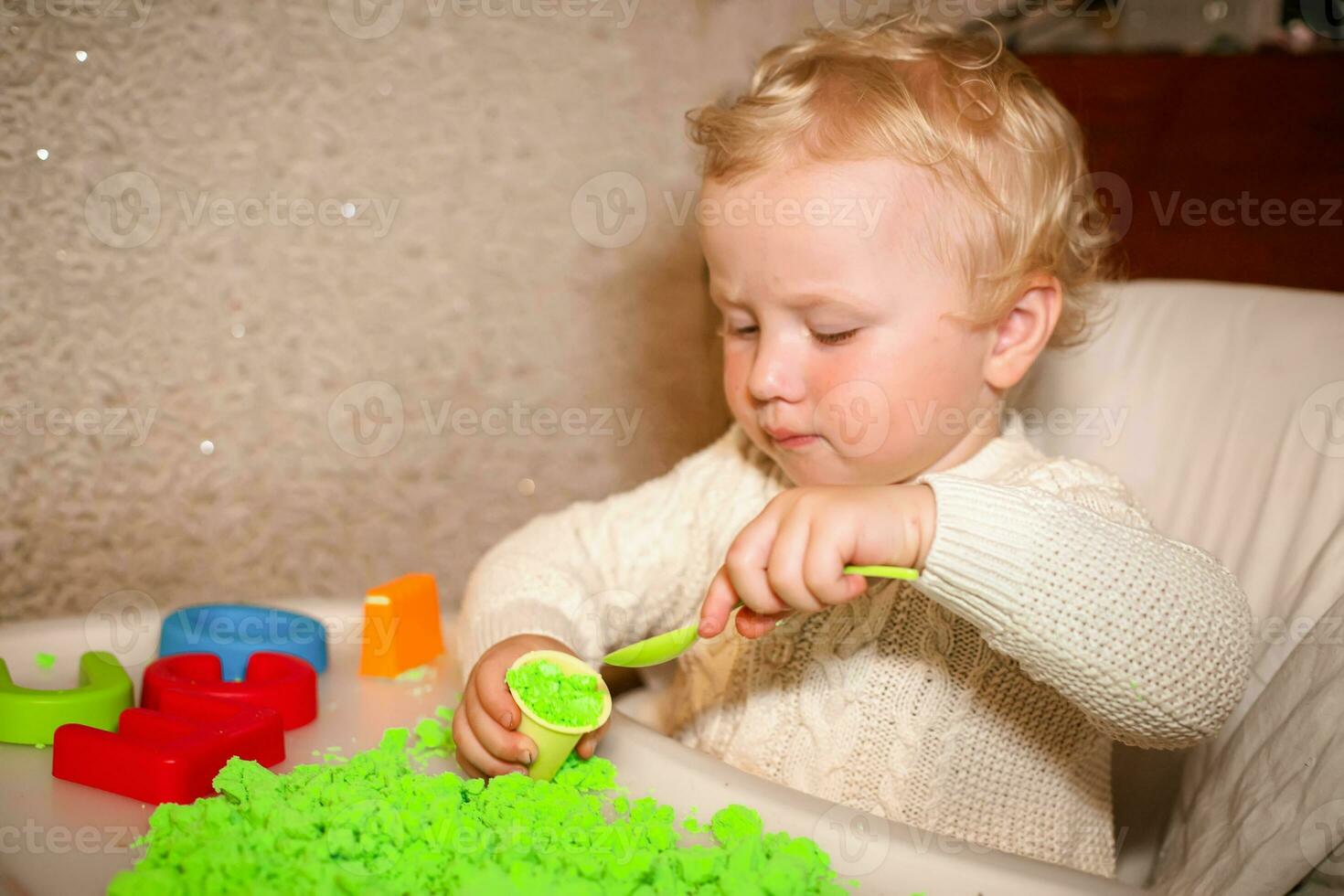 baby holds mold for playing with sand at home. Educational toys for children up to year. girl plays with kinetic sand. child builds shepherds in form of letters of sand. Early development of children. photo