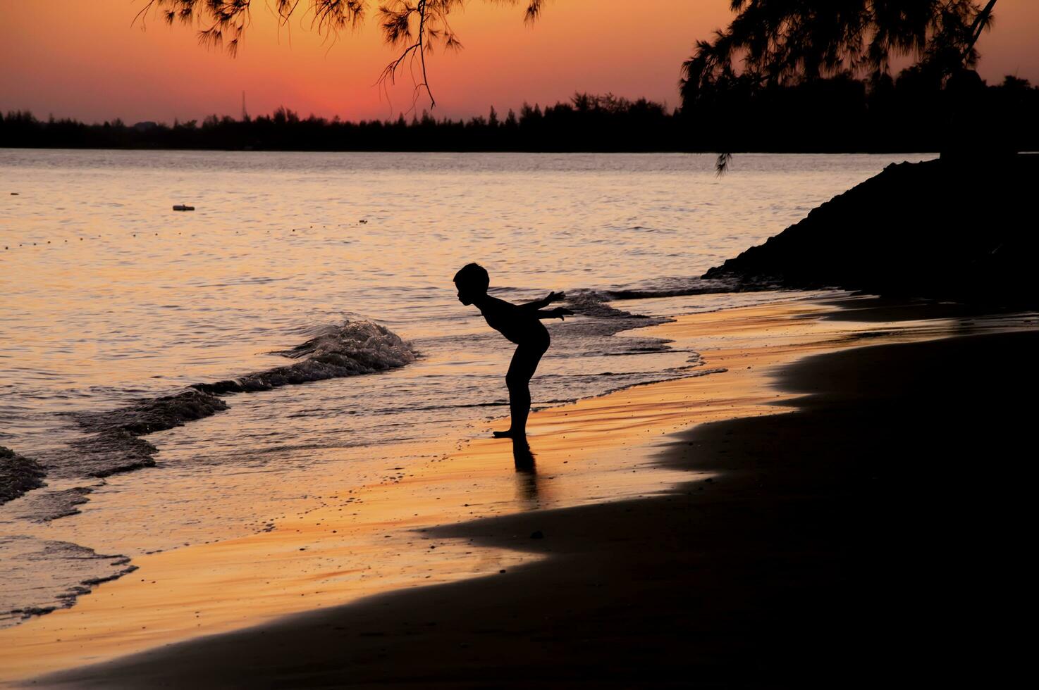 Silhouette of boy standing on the beach at sunset photo