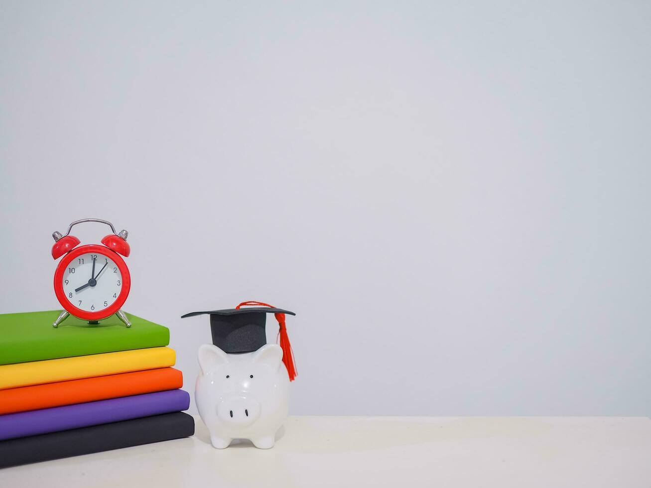 Red alarm on stack hardcover book, Piggy bank with graduation hat, Copy space for text, Back to school, Education concept photo