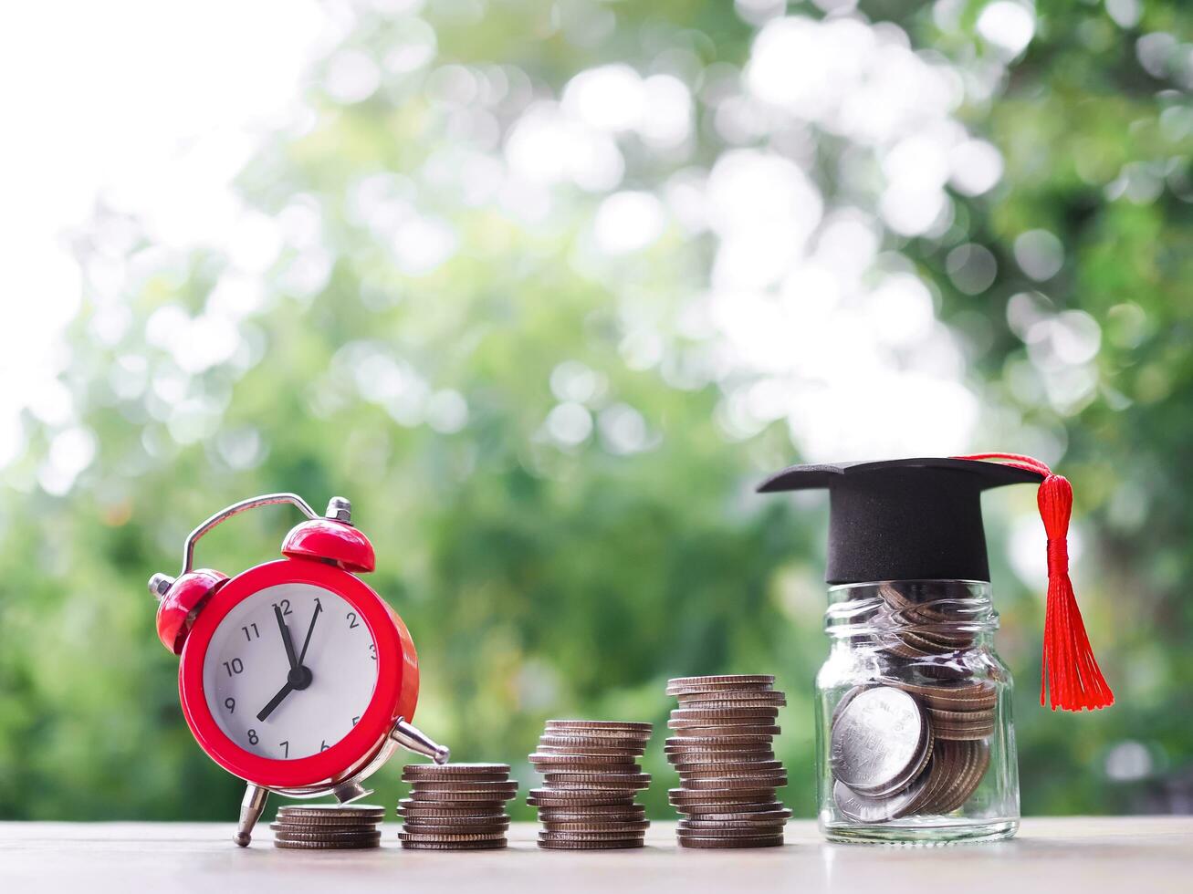 Glass bottle with graduation hat and red alarm on stack of coins. The concept of saving money for education, student loan, scholarship, tuition fees in future photo