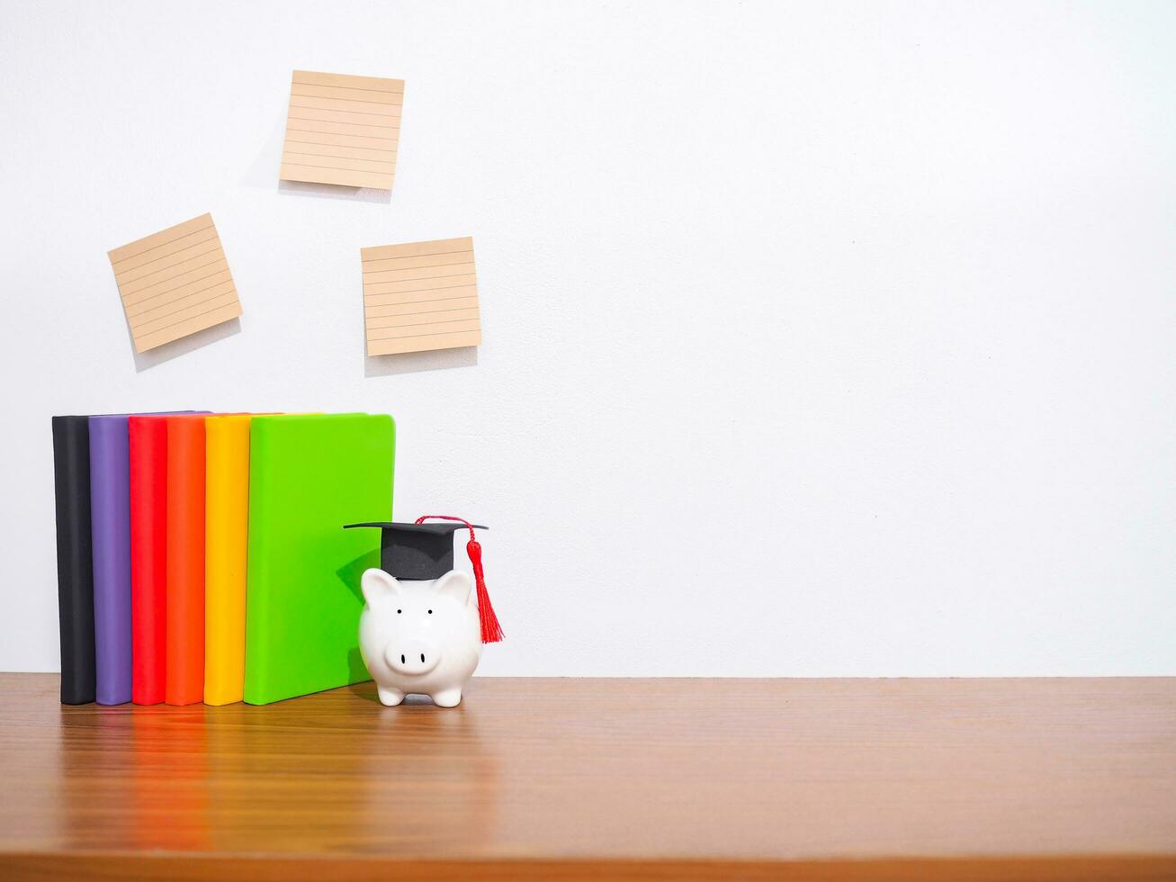 Office desk table, Student creative desktop with colorful hardcover book, Piggy bank with graduation hat, Sticky notes. Copy space for text, Back to school, Education concept photo