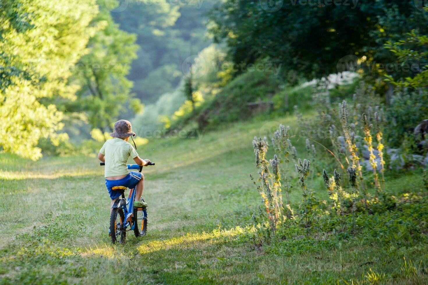 The little boy in a striped suit goes on a forest road. Child in a protective bicycle helmet riding a blue bike. photo