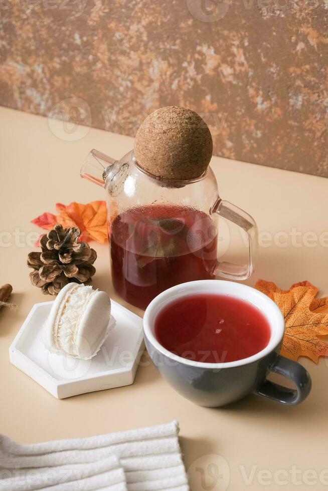 Cup and teapot with cranberry tea and macaroon with an autumn leaf. Autumn warm drink concept photo