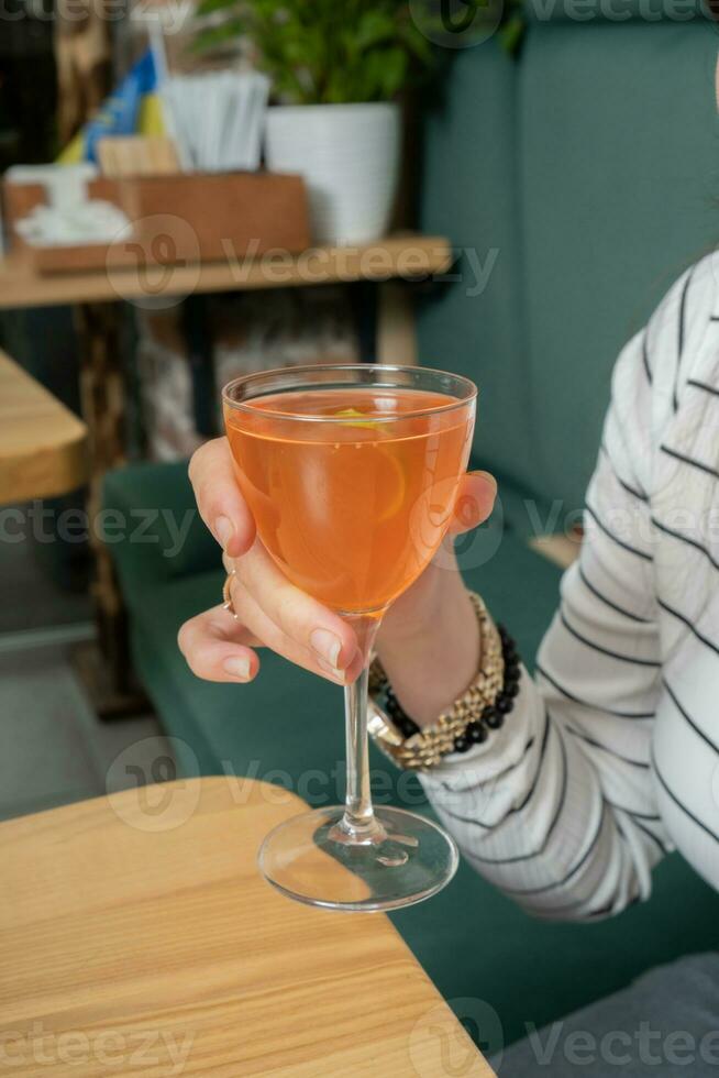 Alcoholic cocktail in hand over a wooden table. Drinking cocktail in cafeteria concept. photo