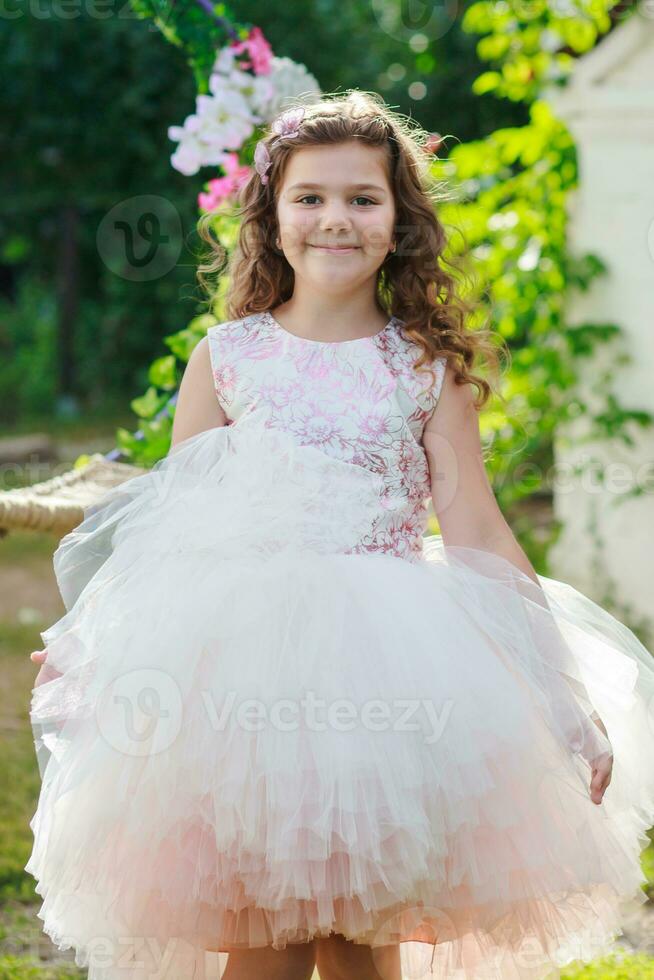 beautiful girl in an elegant pink dress Jumps near swing decorated with flowers. Child Celebrates Birthday 8 Years. beautiful flowers spring theme swing in garden photo