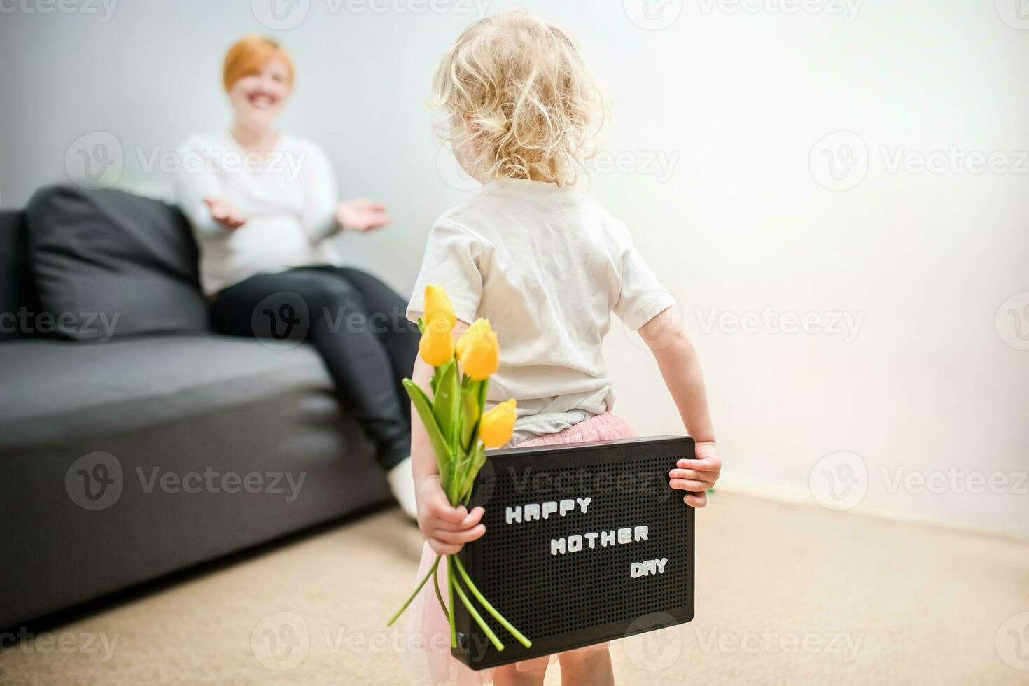 little girl holds a bouquet of yellow tulips and a sign that says Happy Mother's Day. child gives flowers to mother for holiday. photo