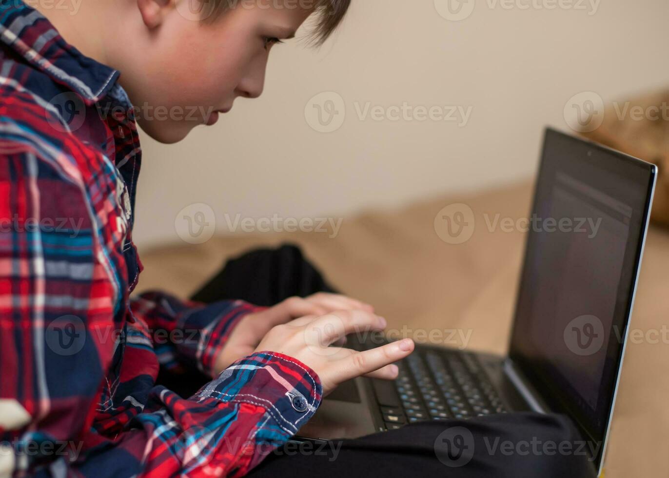 boy in plaid shirt does lessons on laptop. child learns remotely during quarantine of coronavirus. Online learning from home. photo