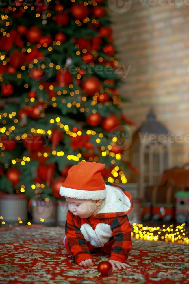 Little surprised child in santa costume in festive room on Christmas eve. Girl on background of Christmas tree. photo