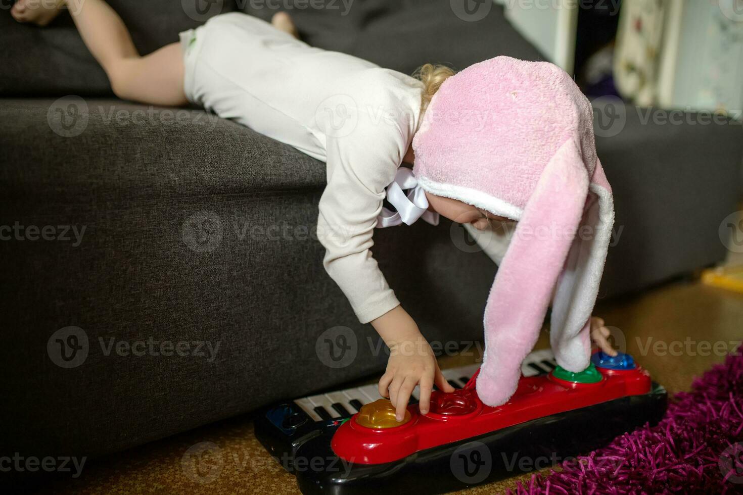 Child playing on synthesizer. A little girl lies on a gray couch and plays with a children's piano. Early music education for little kids, children at school, learning music instruments photo