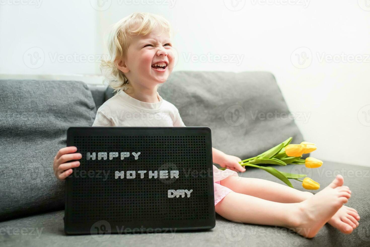 little girl holds a bouquet of yellow tulips and a sign that says Happy Mother's Day. child gives flowers to mother for holiday. photo