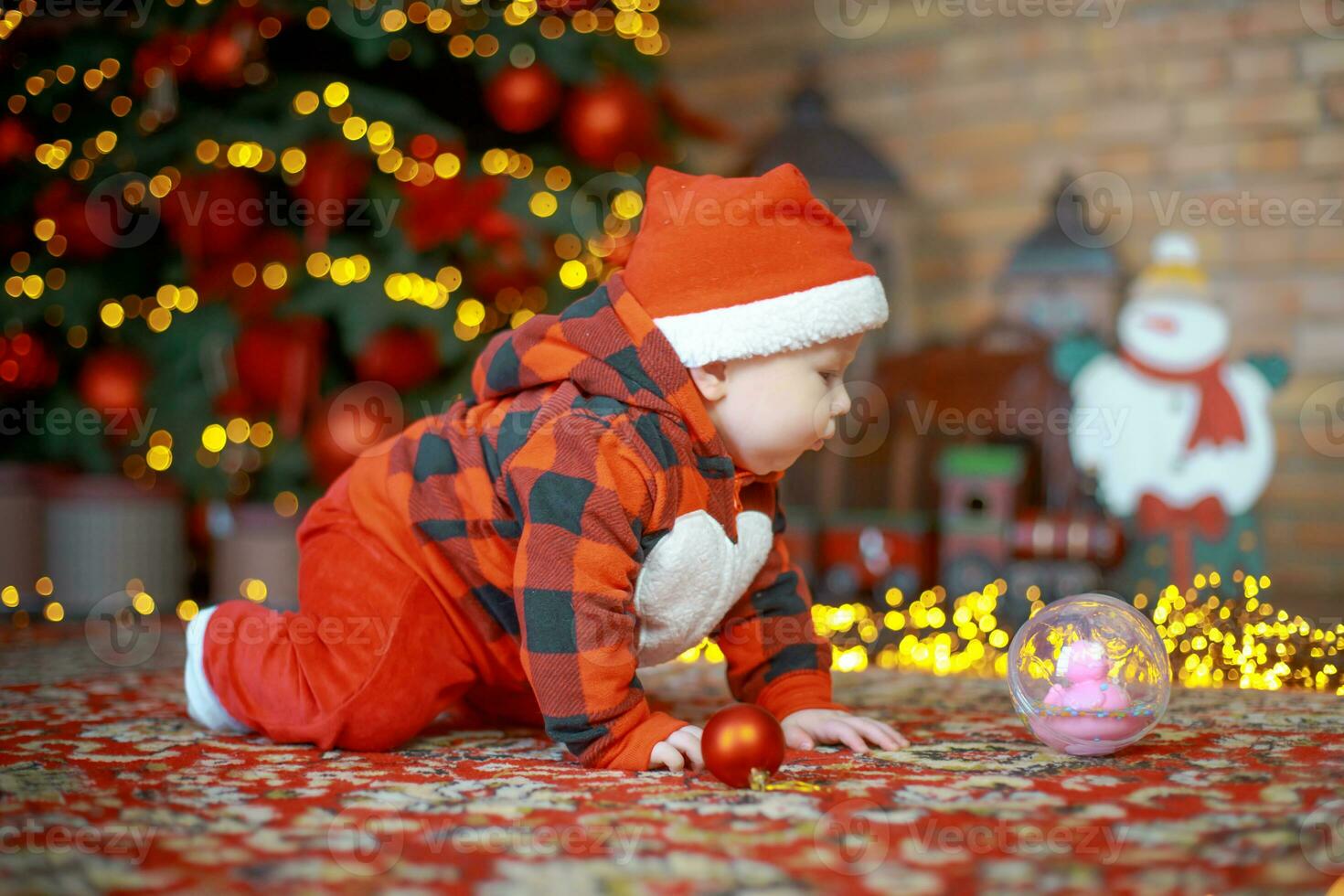 Little surprised child in santa costume in festive room on Christmas eve. Girl on background of Christmas tree. photo