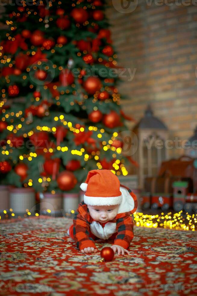 Little surprised child in santa costume in festive room on Christmas eve. Girl on background of Christmas tree. photo