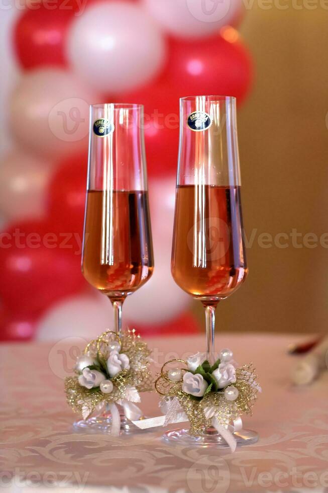 Hands of unknown people who cheering with glasses of champagne against Christmas tree decorated with glowing garland. Blurred background, bokeh. Happy New Year. Close up, slow motion photo