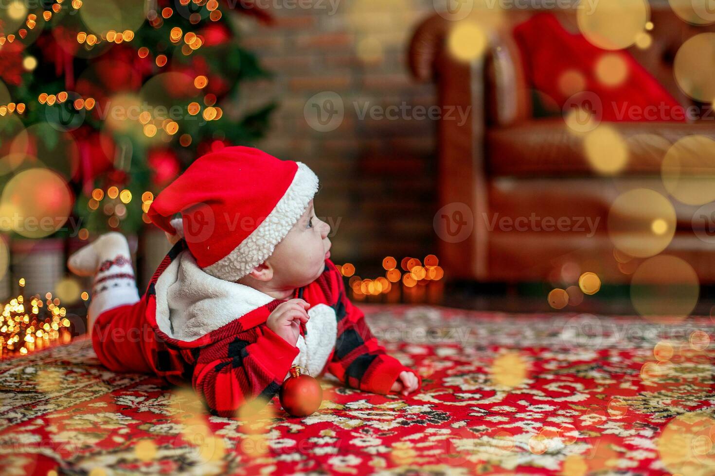 Little six month old baby dressed as Santa Claus. Background for christmas card. The child looks up at the place for inscription. photo