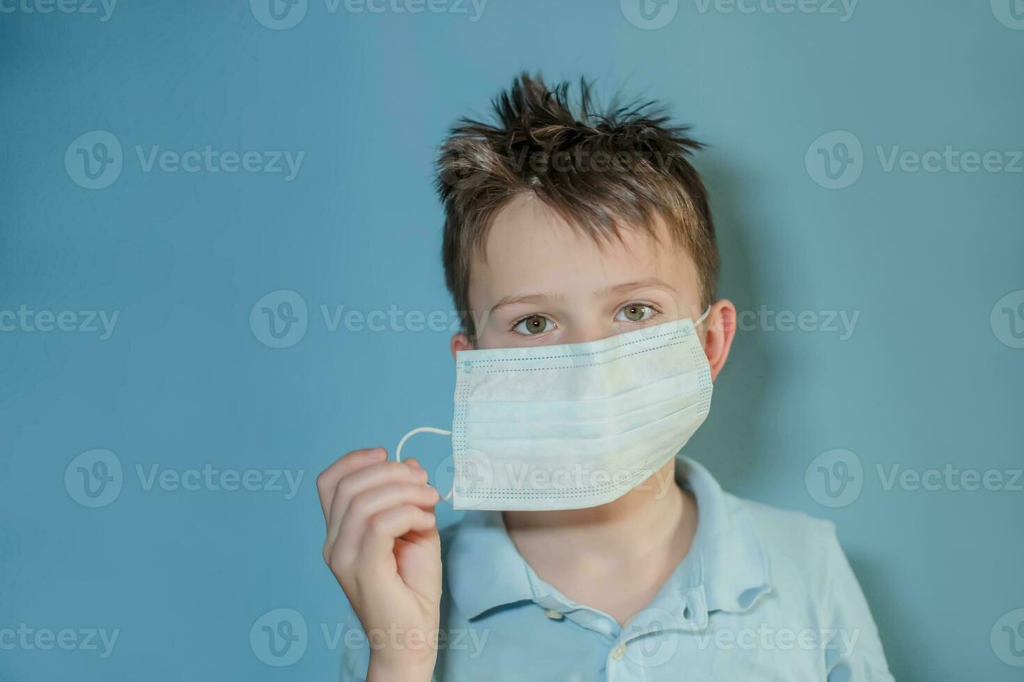 Boy teen takes off medical mask on blue background. child with flu, influenza or cold protected from viruses, pollution in bad epidemic situation, among patients with coronavirus photo