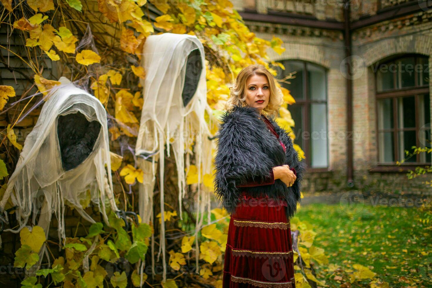 Beautiful woman in a witch costume stands on a background of ghosts. Stylized Halloween decor. photo