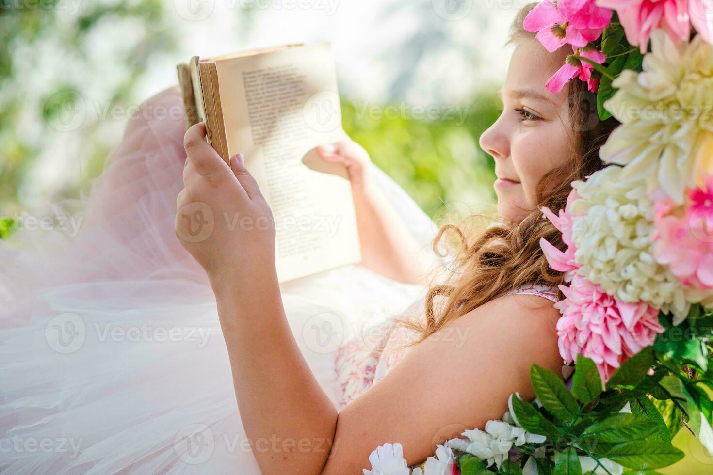 hermosa niña es acostado en columpio con libro en manos. niño lee libros en naturaleza. foto