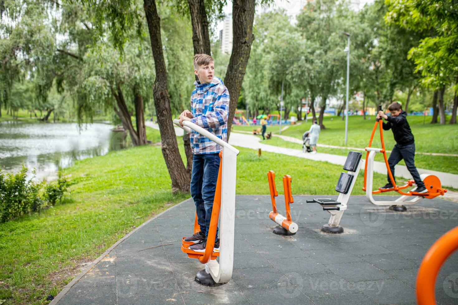 Boys on Outdoor exercise machine FEET SPREEDING in casual clothes doing fitness exercises on outdoor simulators, stretching their legs on a sports ground in a city park photo