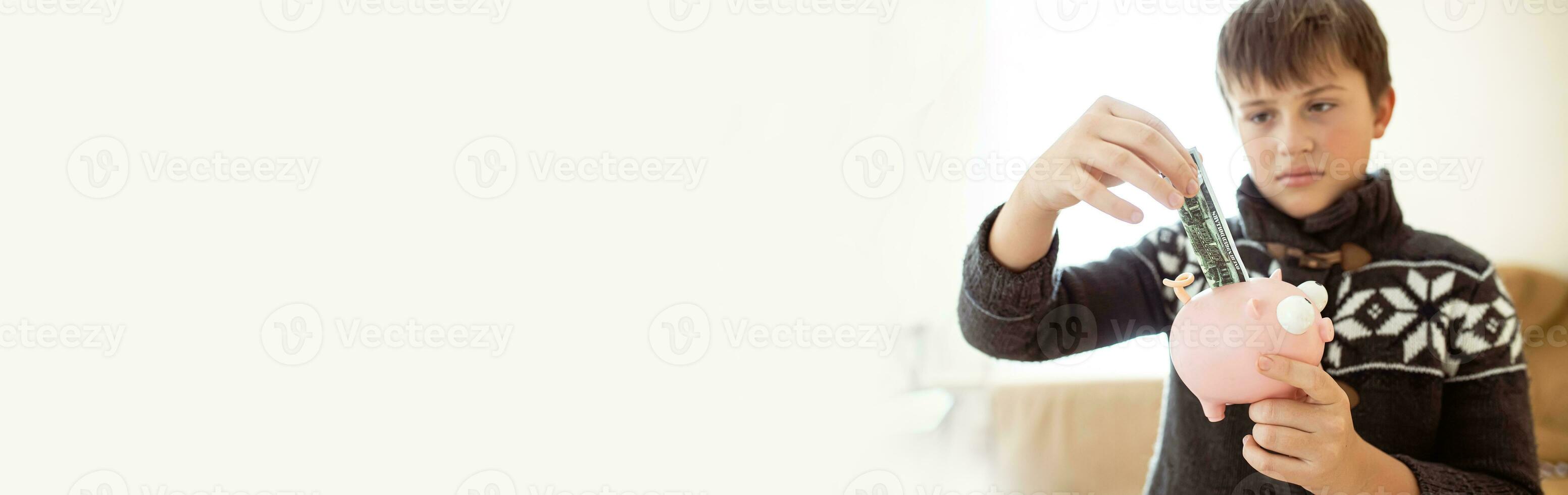 boy shoves a banknote into a piggy bank. Teenager saves money. teenager demanding money to save money. Personal expenses of schoolchildren. photo