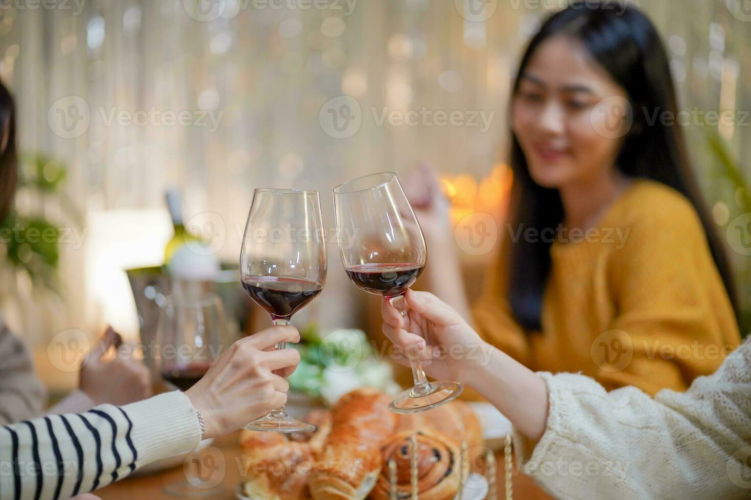 Cheerful friends enjoying home Birthday holiday party. Asian sister cheering drinking red wine celebrating with Birthday cake. photo