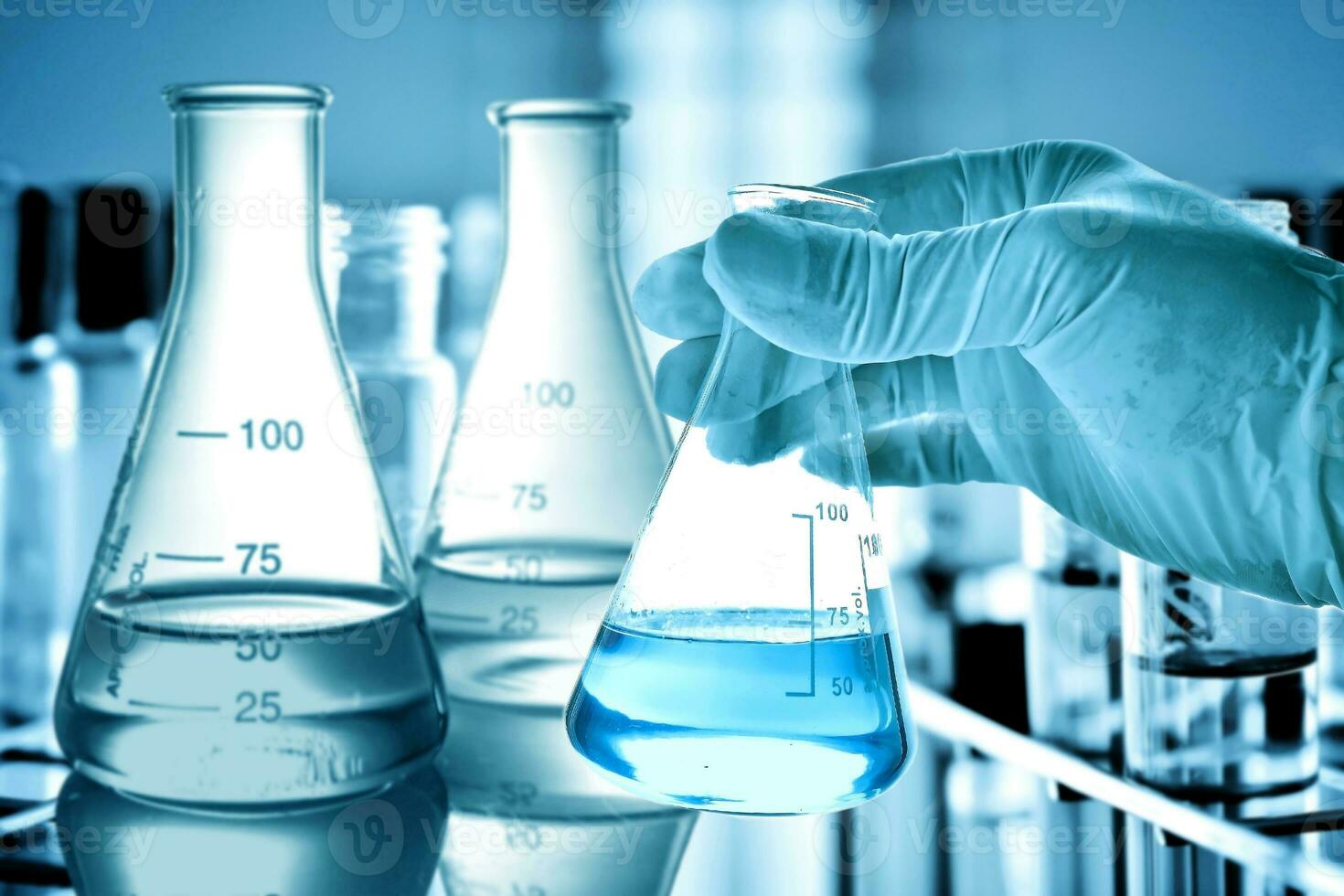 Flask in scientist hand with lab glassware background photo