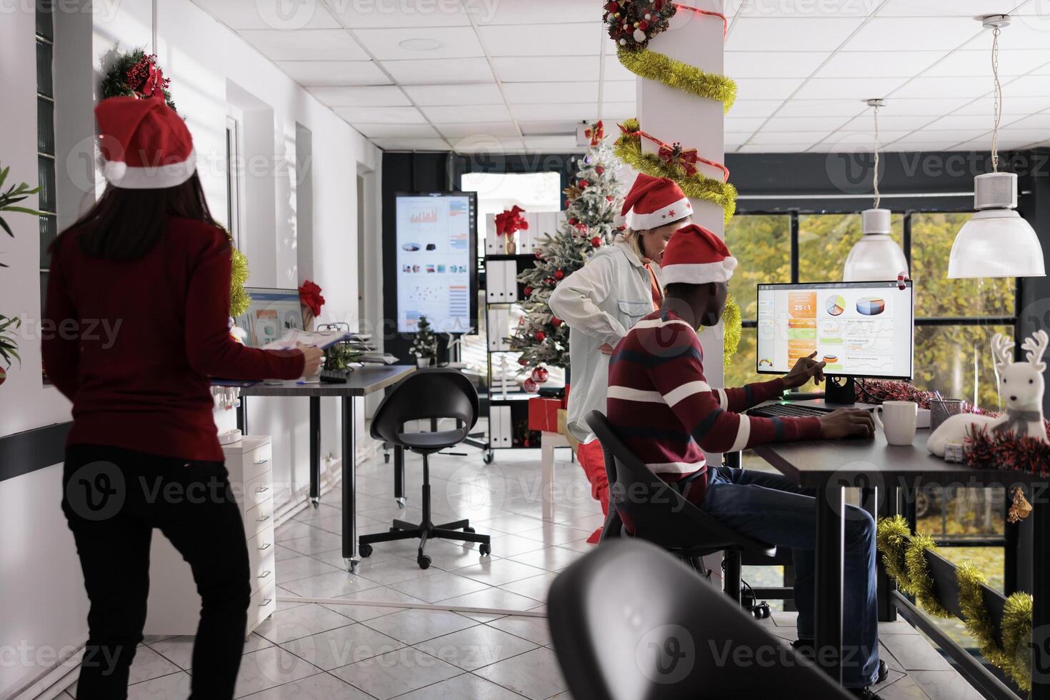 Multiethnical business team working with graphs in festive decorated office during Christmas season. Hard working employees checking accounting diagrams around xmas holiday photo