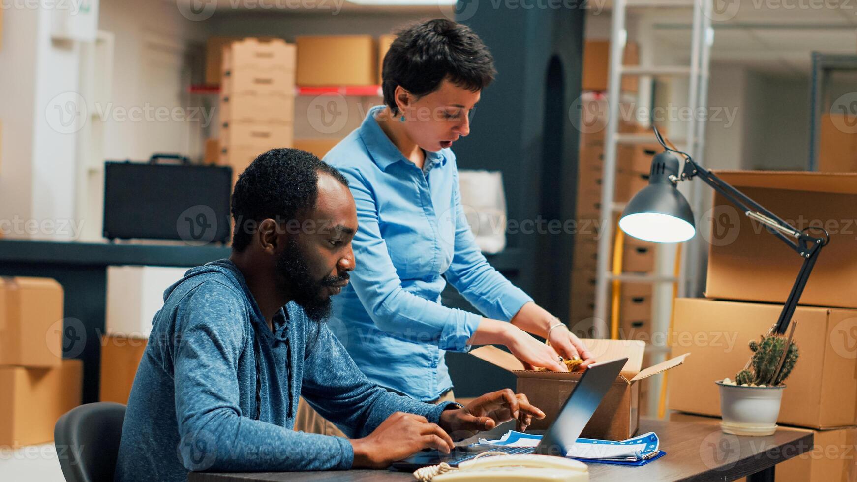 Small business owners doing distribution quality control for startup development, working on stock shipment with laptop at warehouse. Young people doing teamork to ship merchandise. Handheld shot. photo